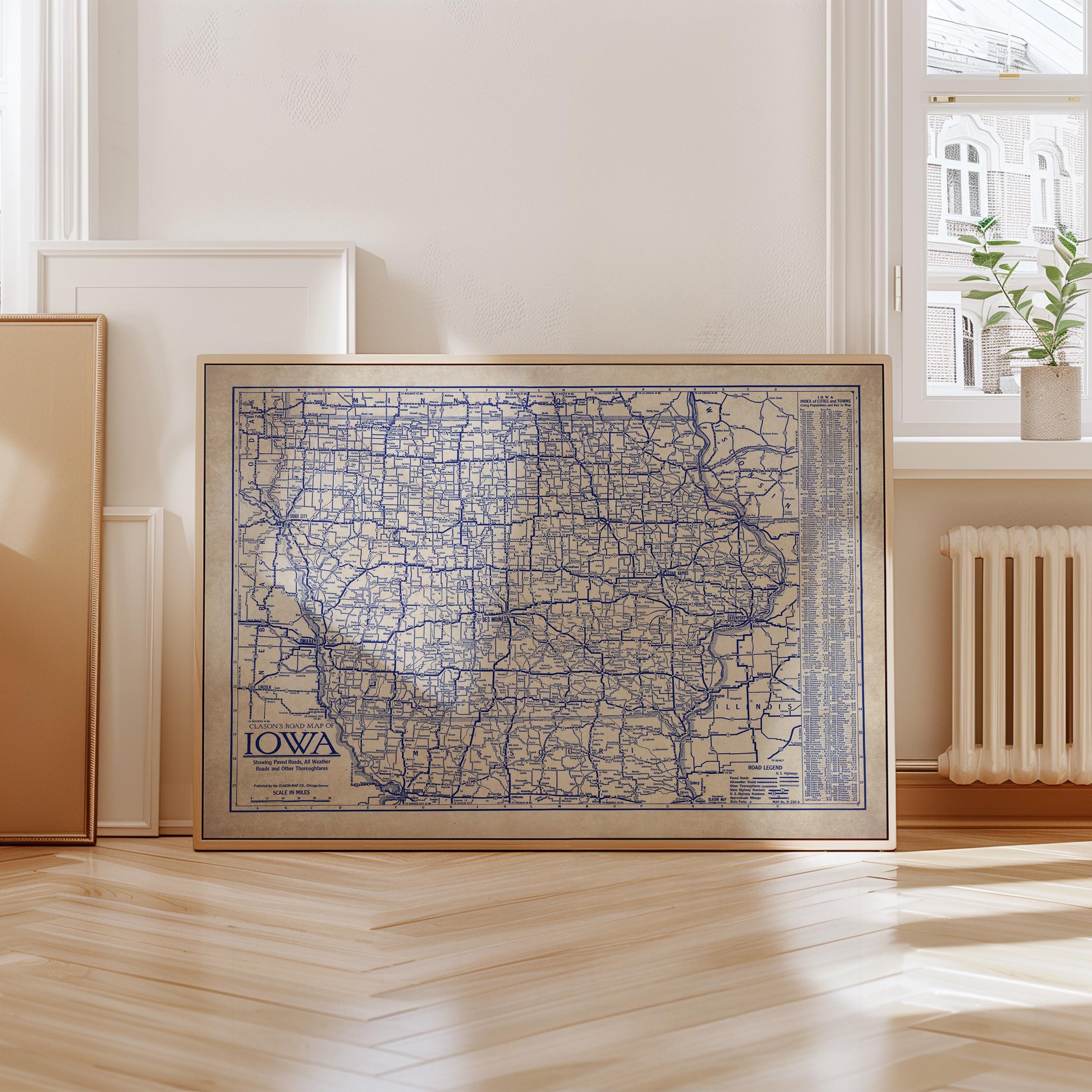 A framed map of Iowa, with a detailed blue and white color scheme, is displayed on a wooden floor in a room with a window and a radiator.