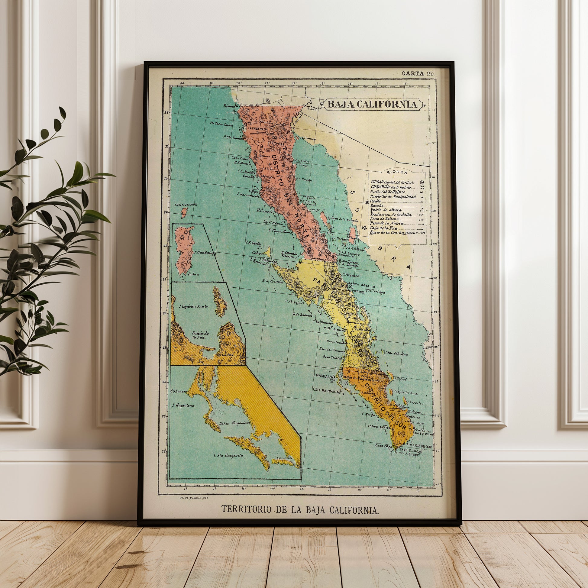 A framed vintage map of California, titled "Caja de la Baja California", is displayed on a wooden floor against a white wall.