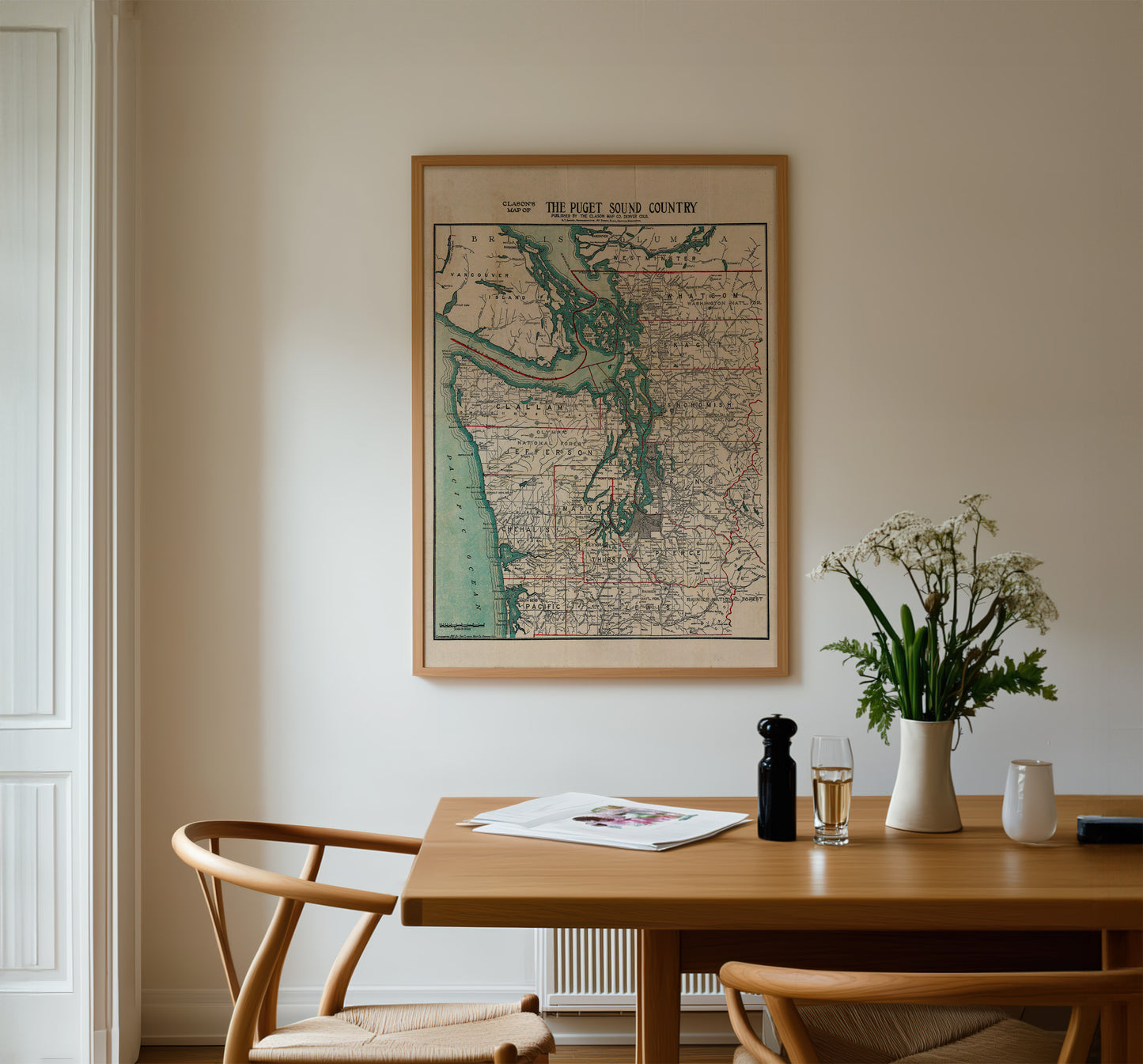 a wooden dining table with a vase of white flowers, a newspaper, and a glass of wine. Above the table, there is a framed map of the United States hanging on the wall.