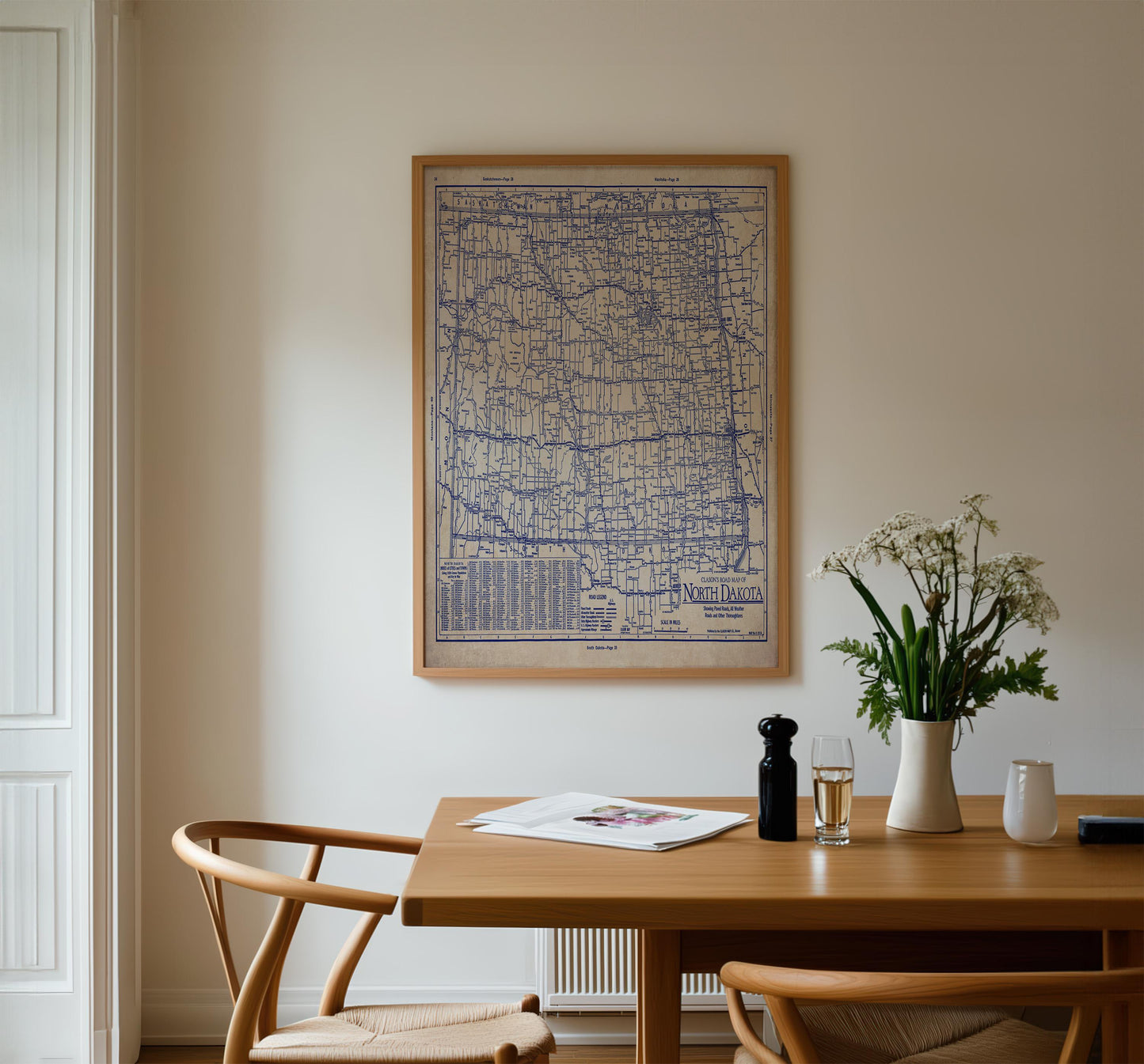 a dining room with a wooden table, two chairs, a framed map on the wall, and a vase of flowers on the table.