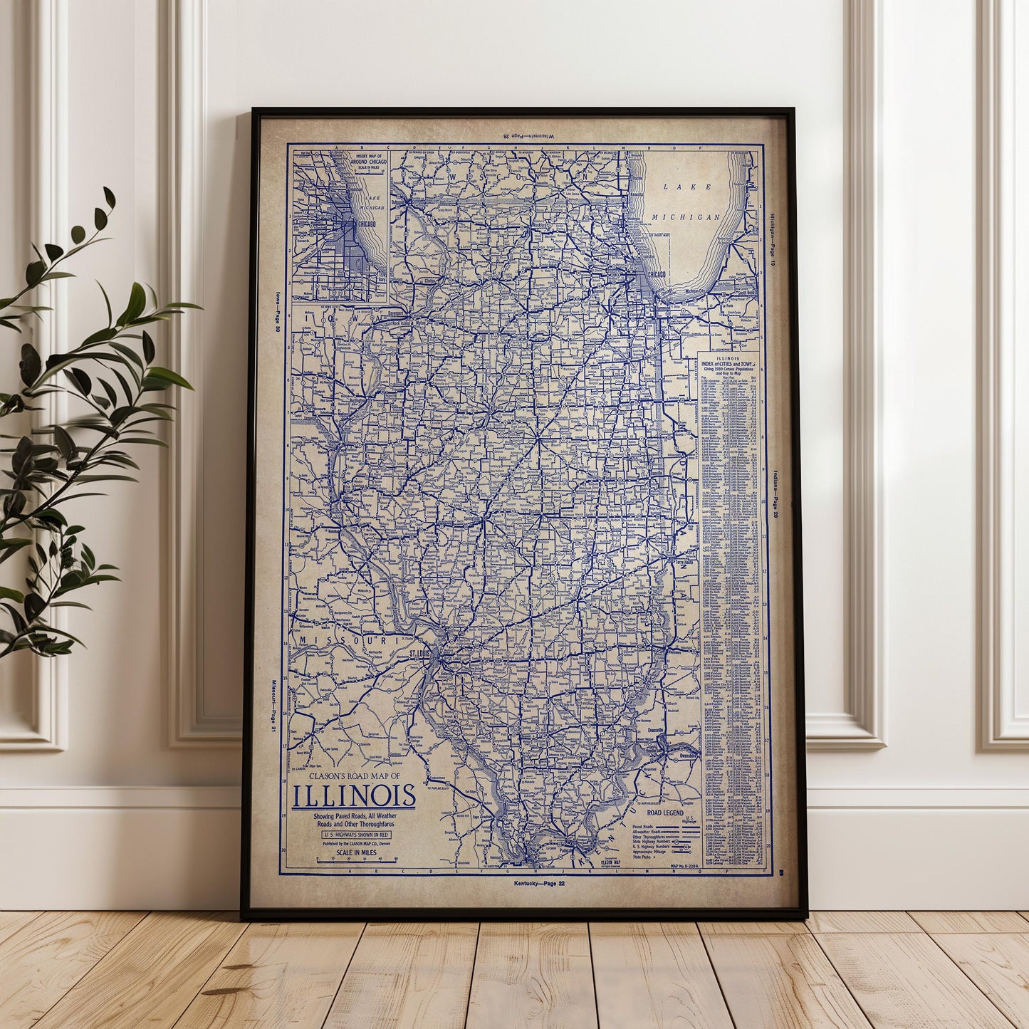 A framed vintage map of Illinois, showing the state's roads and highways, is displayed on a wooden floor against a white wall.