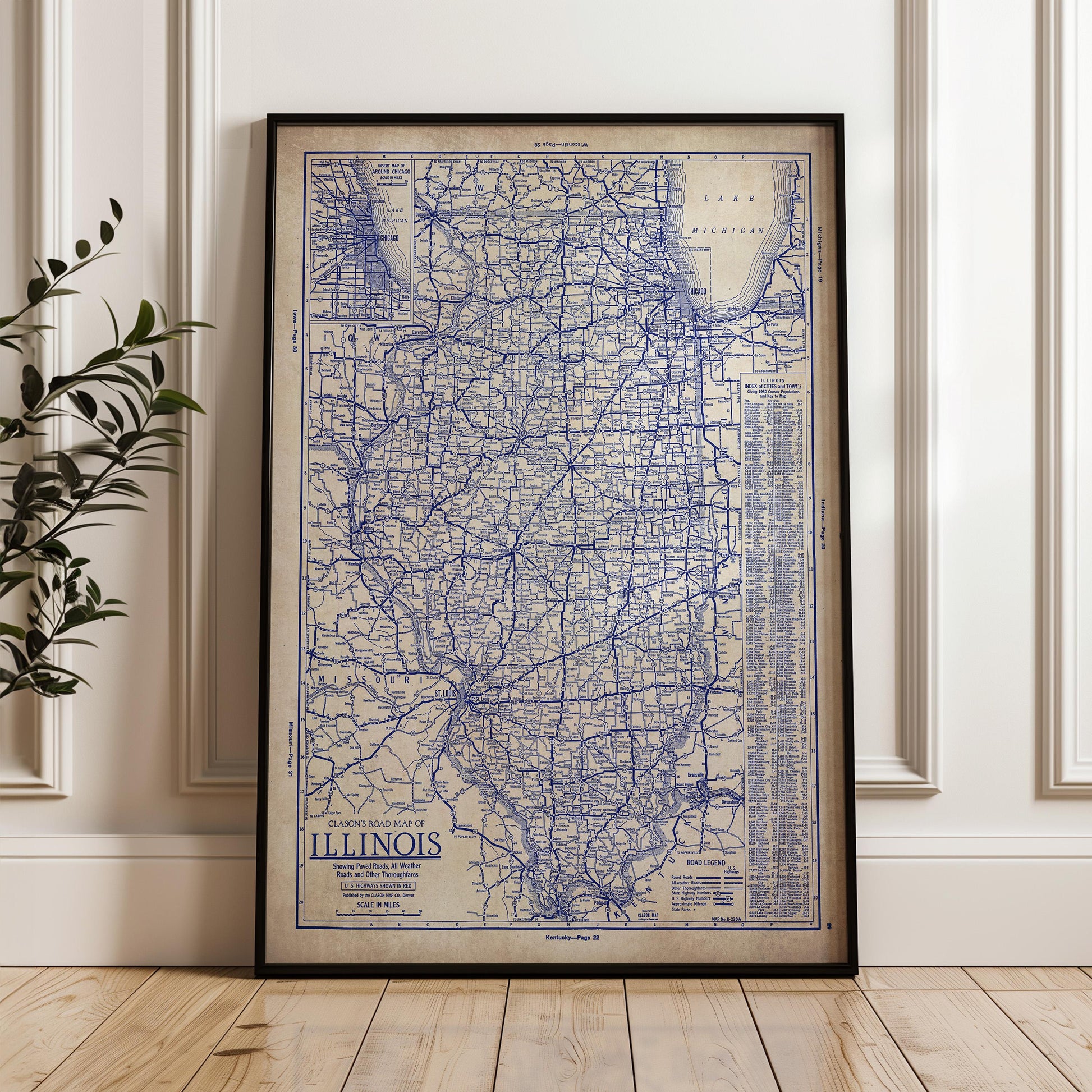A framed vintage map of Illinois, showing the state's roads and highways, is displayed on a wooden floor against a white wall.