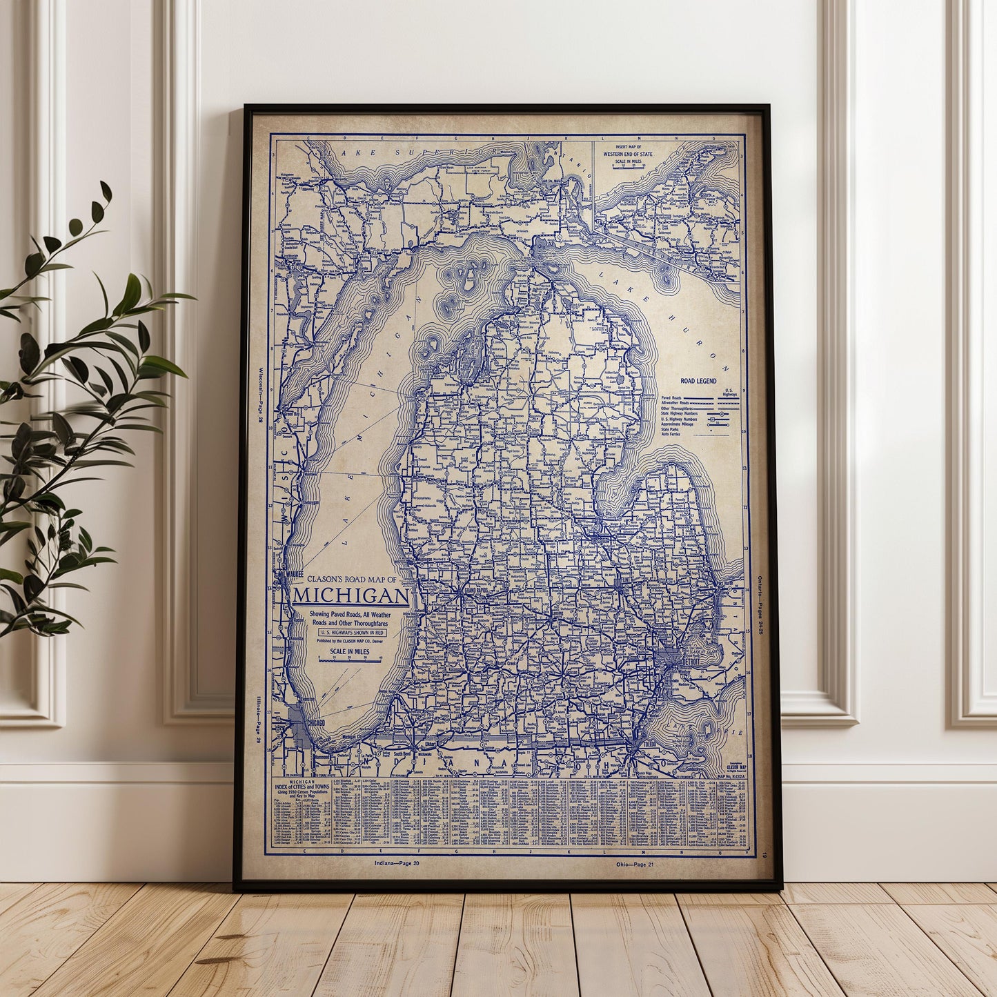 A framed vintage map of Michigan, showing the state's roads and highways, is displayed on a wooden floor against a white wall.