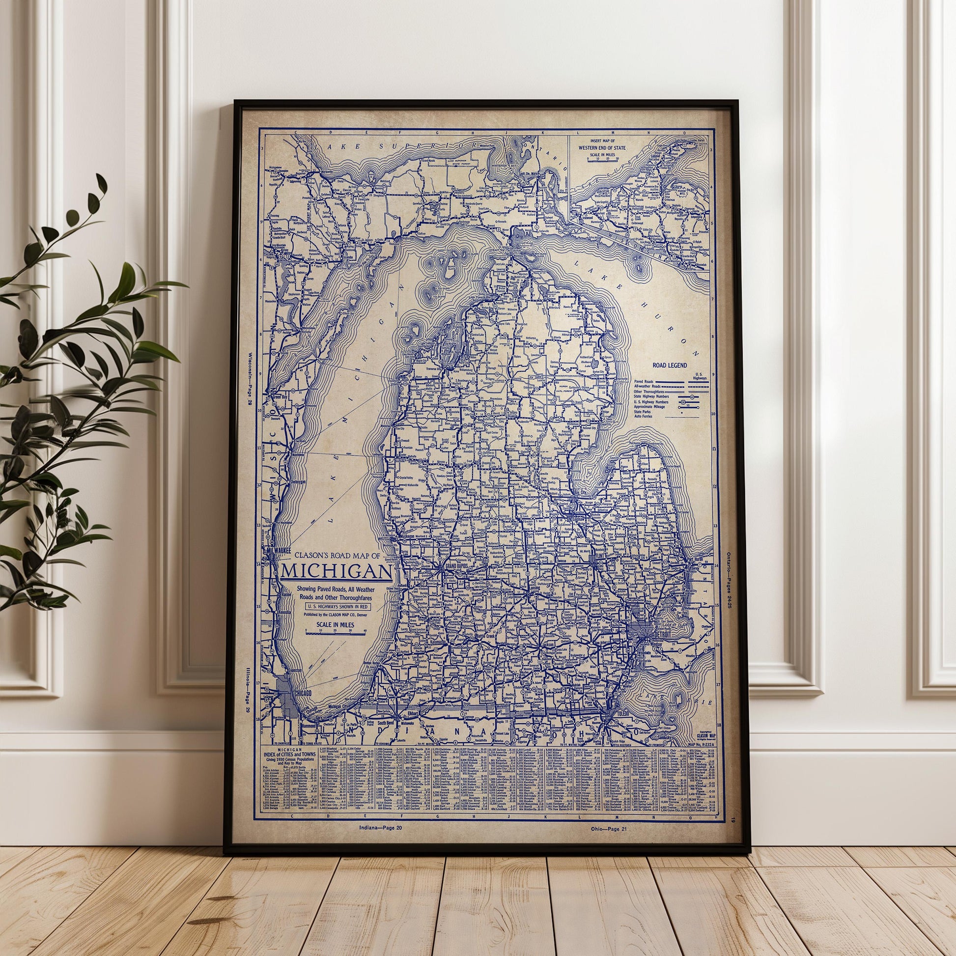 A framed vintage map of Michigan, showing the state's roads and highways, is displayed on a wooden floor against a white wall.