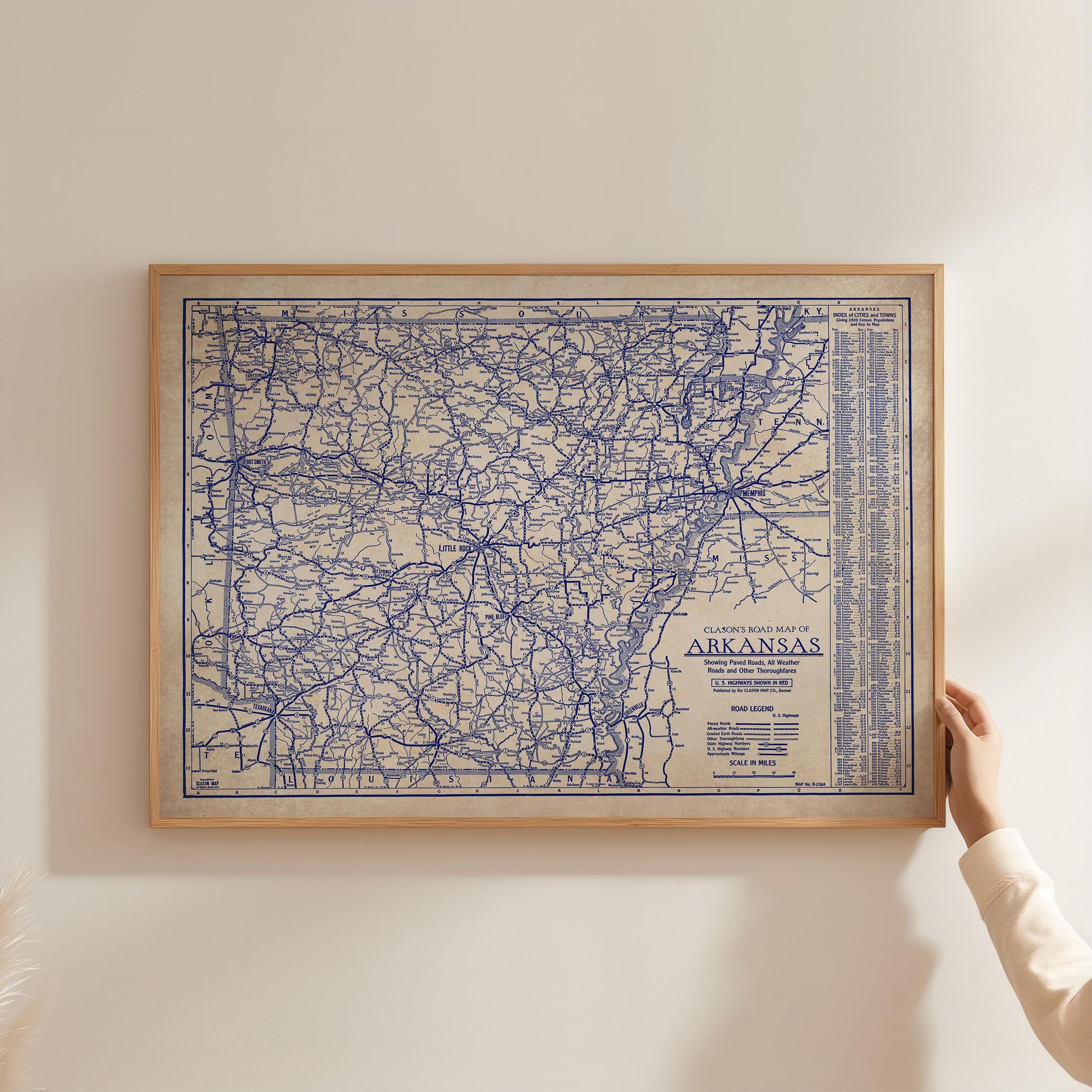 A framed map of Arkansas is being held up against a white wall.